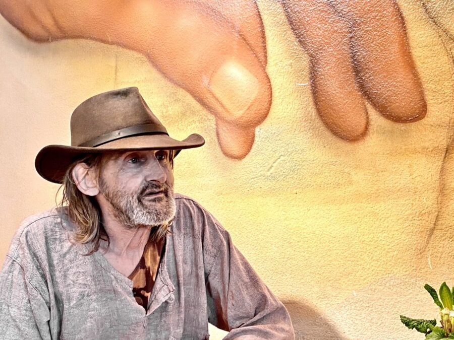Ein Bewohner des Haus Spalen sitzt mit Cowboy Hut gemütlich da. Im Hintergrund ist eine Wand mit Graffitiy, das eine Hand zeigt.