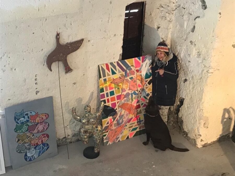 Priska Schwab steht mit ihrem braunen Labrador vor einem ihrer Bilder und zeigt darauf.