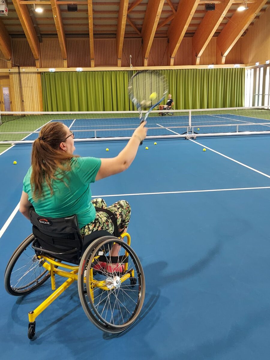 Frau, die im Spezialrollstuhl Tennis spielt.