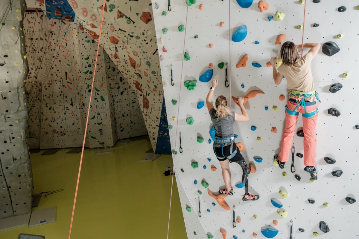 Zwei Frauen klettern an einer Kletterwand. Eine Frau hat eine Beinprothese.