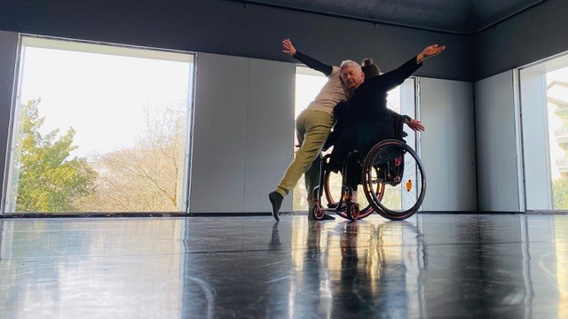 Zwei Personen tanzen miteinander. Eine Person sitzt im Rollstuhl.