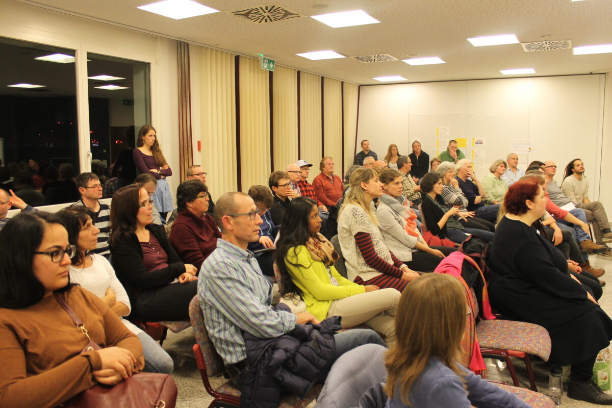 Eine Gruppe von Menschen sitzt in einem Besprechungszimmer und schaut nach vorne.