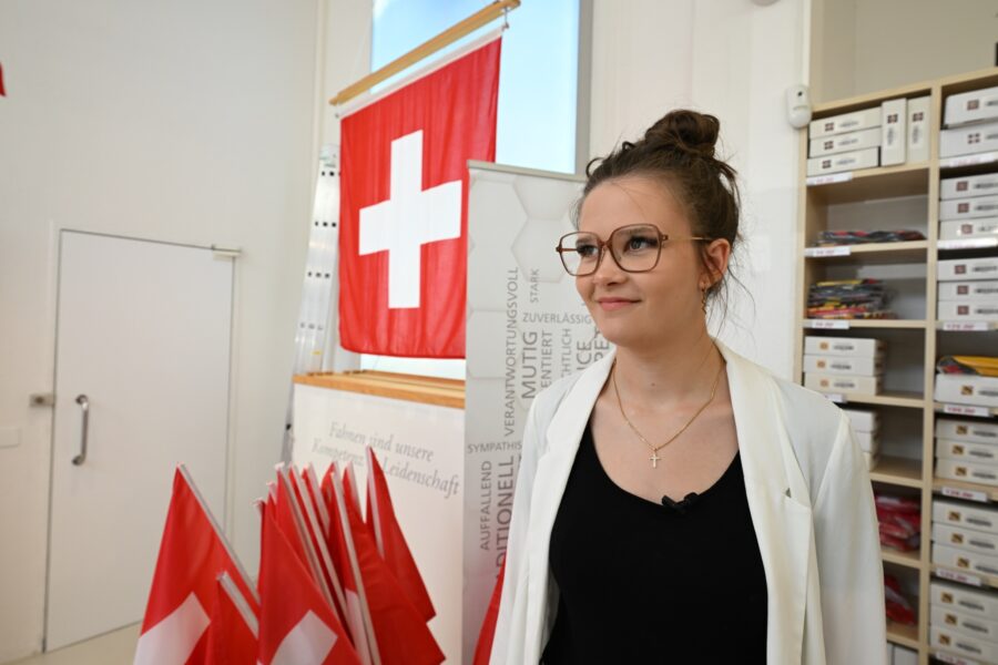 Eine Frau mit Brille. Im Hintergrund hängt eine Schweizerfahne.