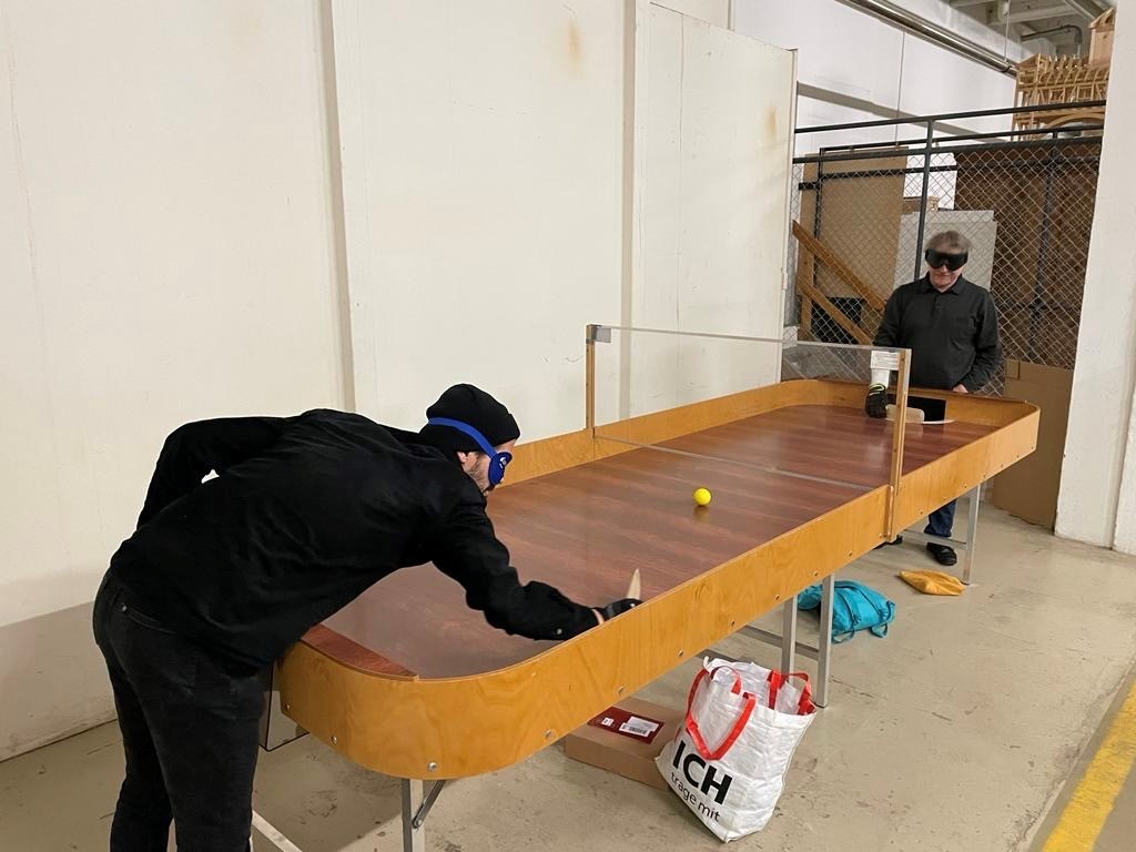 Zwei Spieler mit einer Dunkelbrille spielen Showdown auf einem Tisch mit Umrandung und versuchen ein Tor zu erzielen.