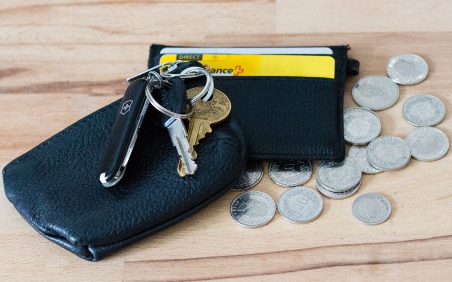 Auf dem Bild sind ein Geldbeutel, ein Schlüsselbund und mehrere Münzen zu sehen.