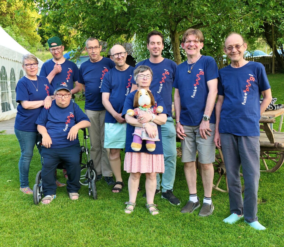 Ein Gruppe von neun Menschen. Es sind die MusikerInnen der Band Funkesprung. Sie stehen auf einer Wiese. Sie tragen T-Shirts mit dem Bandnamen darauf.