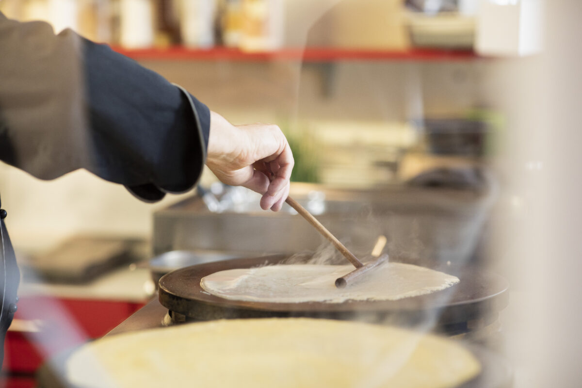 Ein Mensch, der Crêpes zubereitet. Man sieht nur seinen Arm sowie die beiden Crêpes, die erwärmt werden.