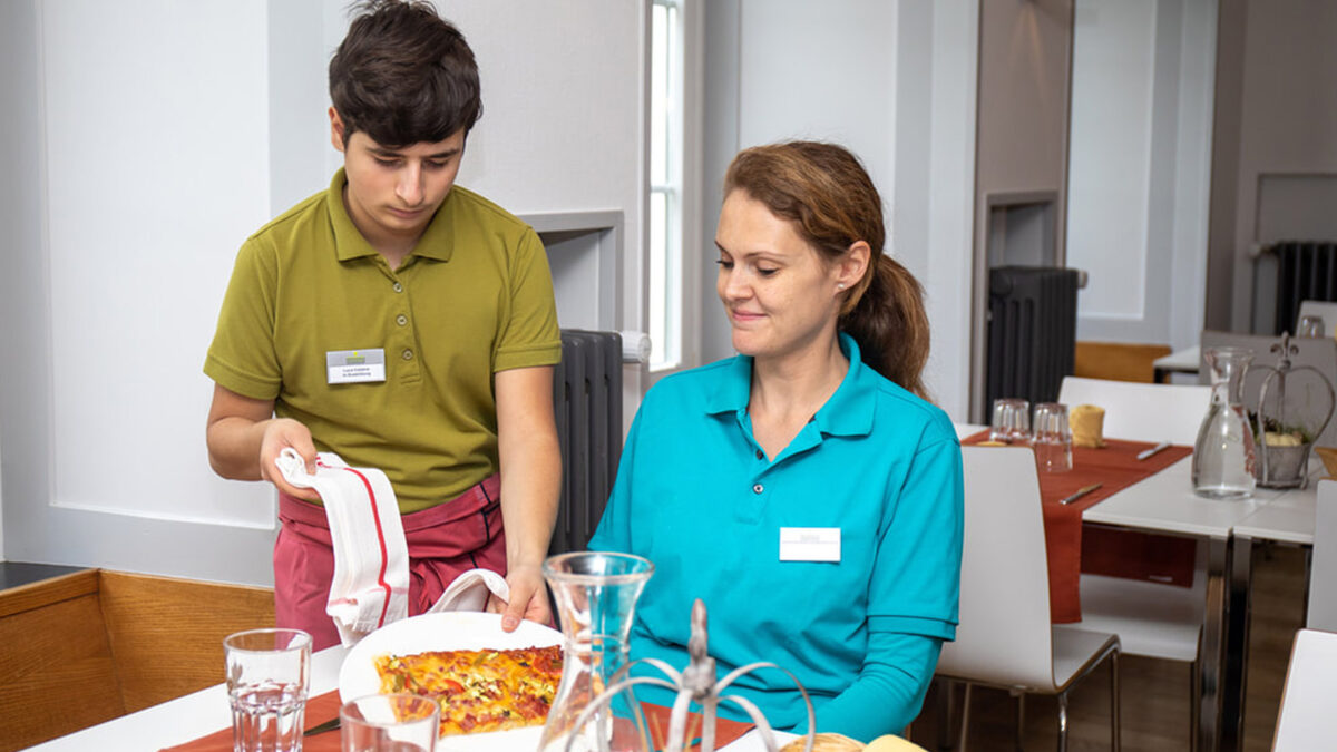 Ein junger Mann serviert einer Frau was zu Essen.