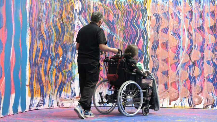 Ein Mann assistiert einen Menschen im Rollstuhl im Museum.