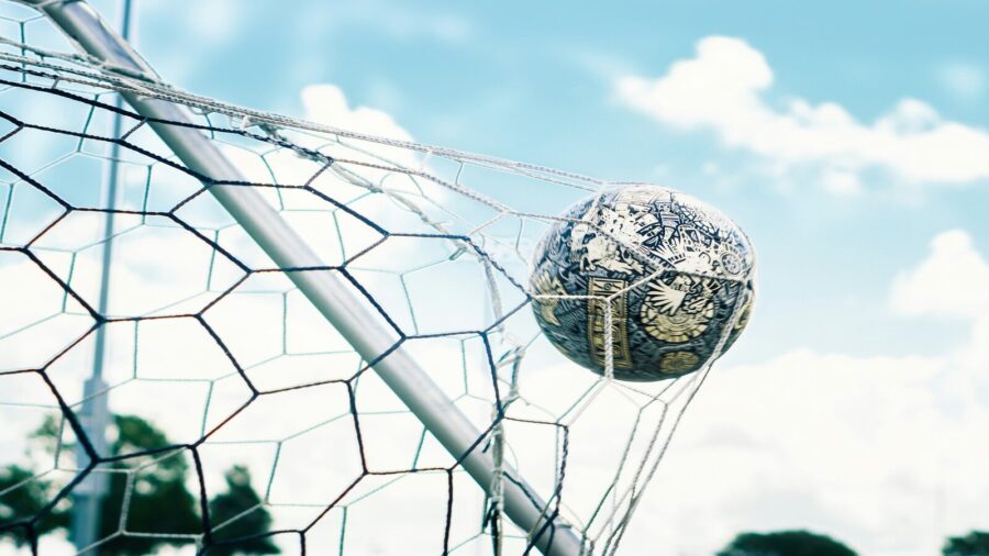 TOR! Ein Fussball dreht sich in den Maschen des Tornetzes. Im Hintergrund ist der blaue Himmel zu sehen. Ein perfekter Tag für ein Fussballspiel.