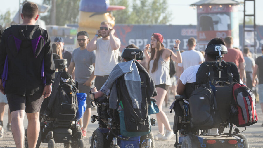 Drei Menschen im Elektrorollstuhl fahren an einem Festival durch die Menschenmenge.