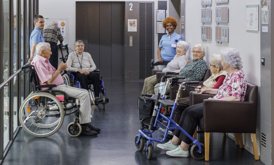 Fünf Bewohnerinnen und ein Bewohner sitzen in einem Alterszentrum auf einen Schwatz im Gang gemütlich zusammen. Der Mann und eine Frau sitzen im Rollstuhl, zwei Frauen nutzen einen Rollator.