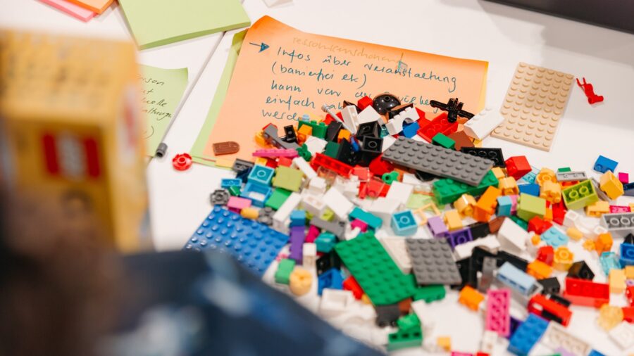 auf dem Bild liegen viele Legosteine und unterschiedlichen Farben, Formen und Grössen. Es ist ein Zettel zu sehen, auf dem Notizen stehen.