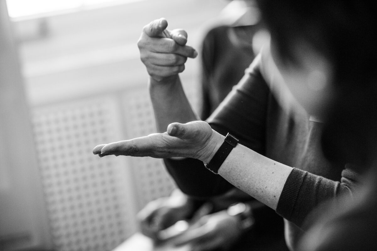 Zwei Personen kommunizieren in Gebärdensprache. Eine Hand zeigt nach vorne, die andere liegt flach offen darunter.